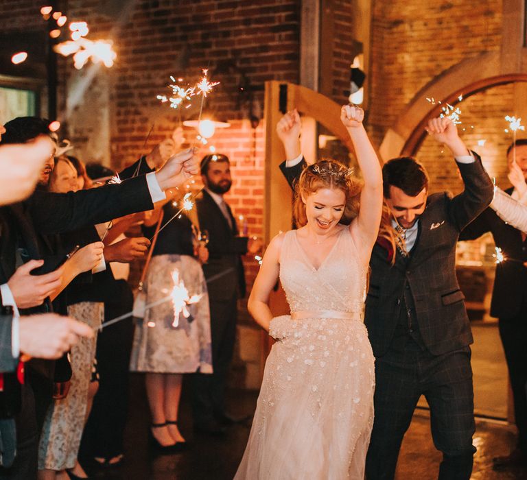 Bride in a blush tulle and pearl wedding dress and bridal crown dancing through the sparkler exit with her husband in a grey suit 