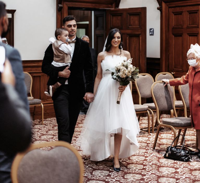 Bride & groom walk down the aisle together with their little boy on the day of their wedding