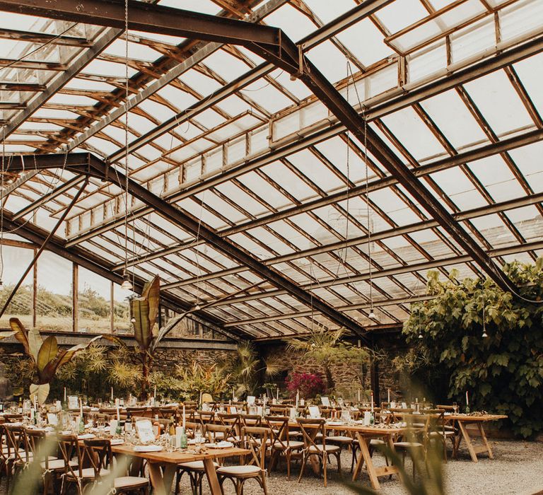 Interior of the glasshouse at Anran Devon set up for a wedding reception with long wooden tables, wooden chairs and candles 