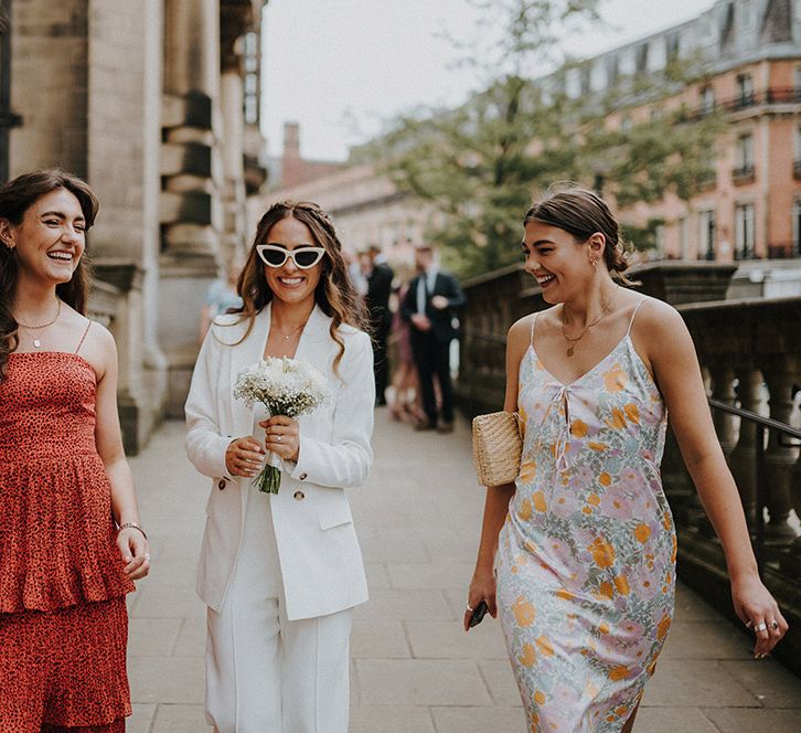 Bride in a Reiss suit and sunglasses holding a white flower bouquet 