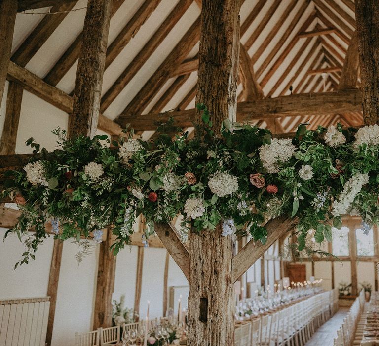 White, green and blush pink floral and foliage garland hung on wooden beams inside Loseley Park for wedding breakfast 