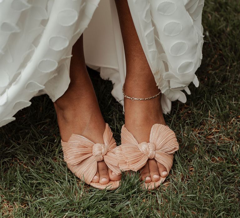 Bride holds up edge of spotted Vagabond wedding dress to show blush pink bow heeled sandals at Wasing Park wedding