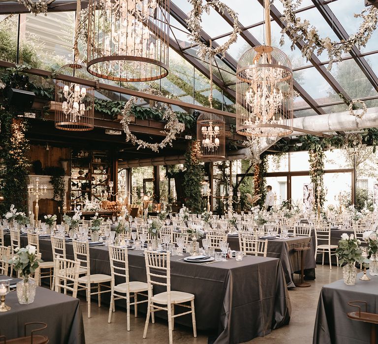 Dark tablecloths line the tables as green foliage lines the windows and large floral installations hang around circles suspended from the ceiling 