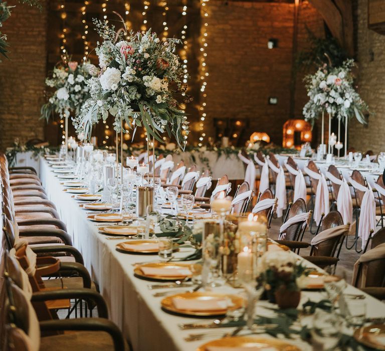 White, pink and green flower bombs on stands at long wedding breakfast table lit with strung fairy lights at Tythe Barn wedding with barn wedding flowers