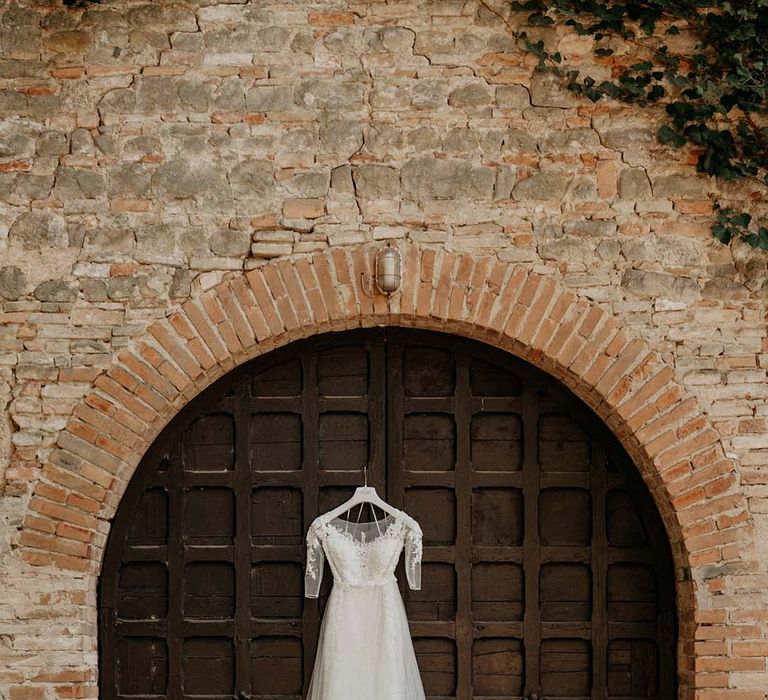 Brides dress hangs up against medieval style door next to brickwork  | Royal Studio