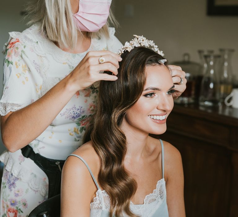 Smiling bride with curled hair has floral headband put on by hair stylist before summer wedding at Primrose Hill Farm 