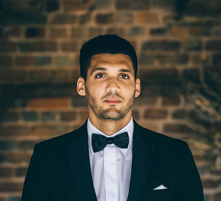 Groom in a three-piece black suit with black bow tie and white pocket square 