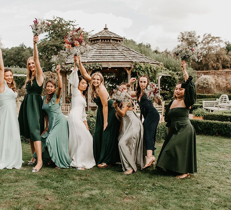 Bride poses with her bridesmaids who wear different styled bridesmaid gowns in differing shades of green