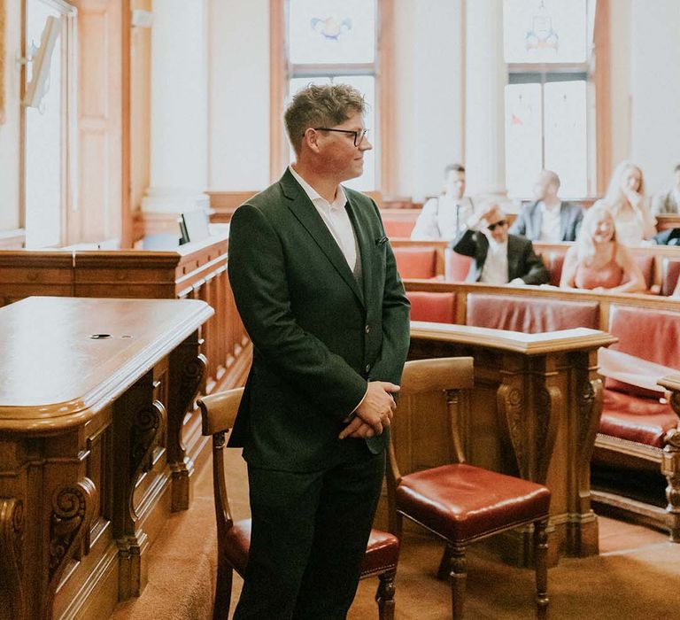 Groom awaits his bride at the altar whilst wearing green jacket and white Nike trainers