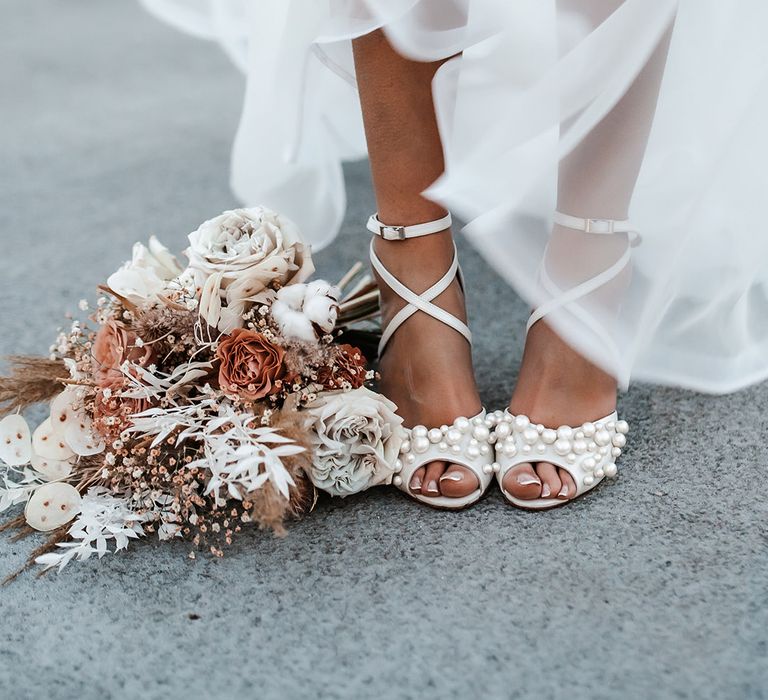 Bride in a Charlotte Mills wedding shoes with pearl detail standing next to her dried flower wedding bouquet 