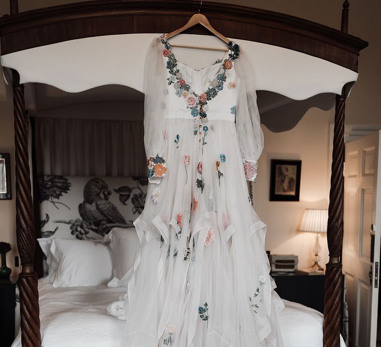 Mesh sleeve embroidered Victoria Sanders wedding dress with floral embroidery hangs from bed