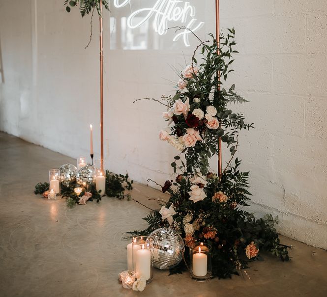 Neon light in front of metal arch way complete with floral decor