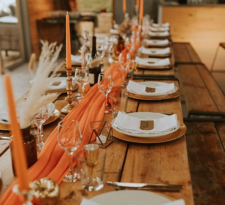 Rustic wooden wedding table with orange table runner, orange dinner candles and rustic wedding table decor