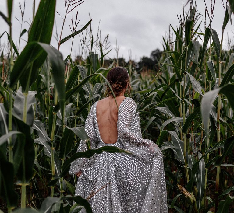 Bride in a silver sequin wedding dress walking through some crops at her home stretch tent wedding 