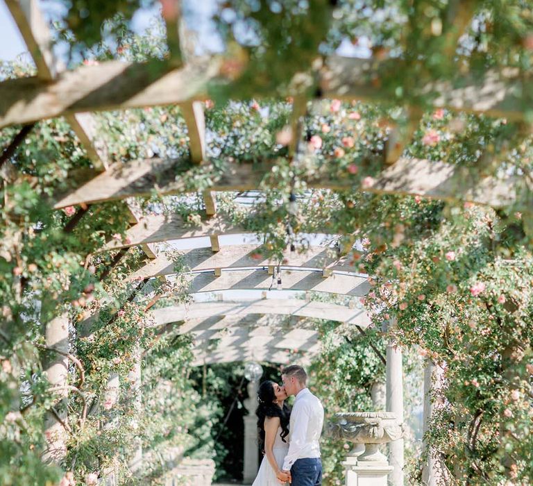 Bride & groom kiss underneath pergola on their wedding day