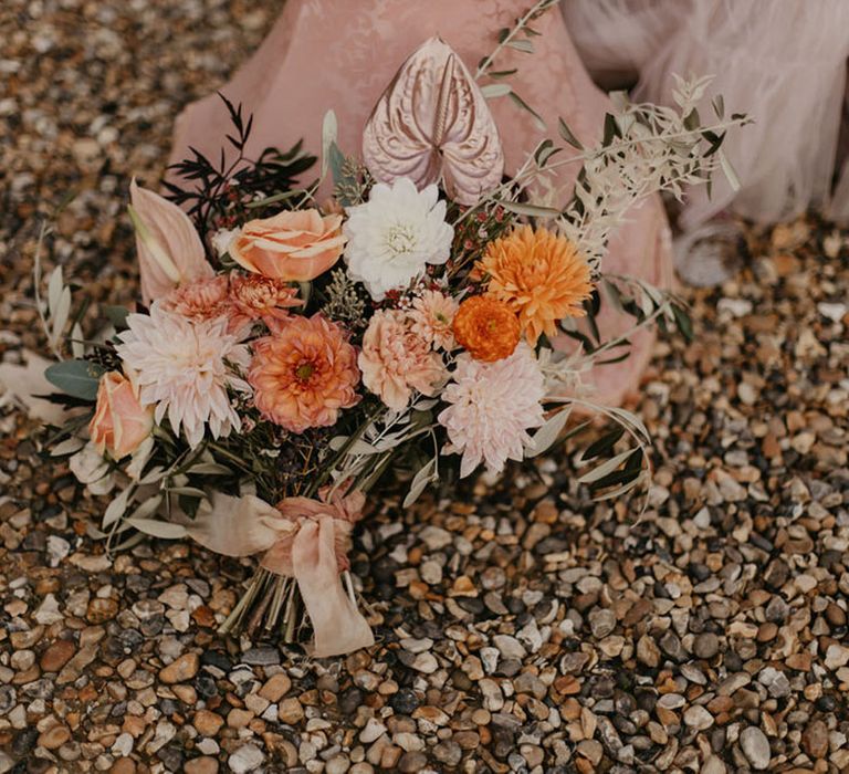 Orange, peach, coral and pink wedding bouquet tied with ribbon including anthuriums, roses and dahlias 