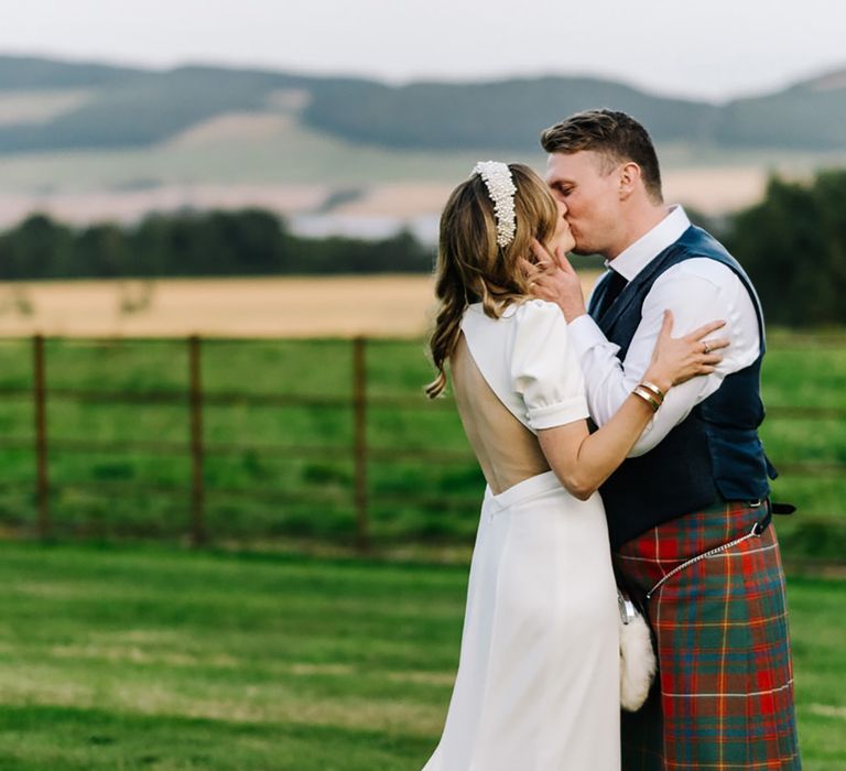 Bon Bride wedding dress with cutout back and puff sleeves with pearl headband worn by bride kissing groom in traditional kilt for Errol Park wedding 