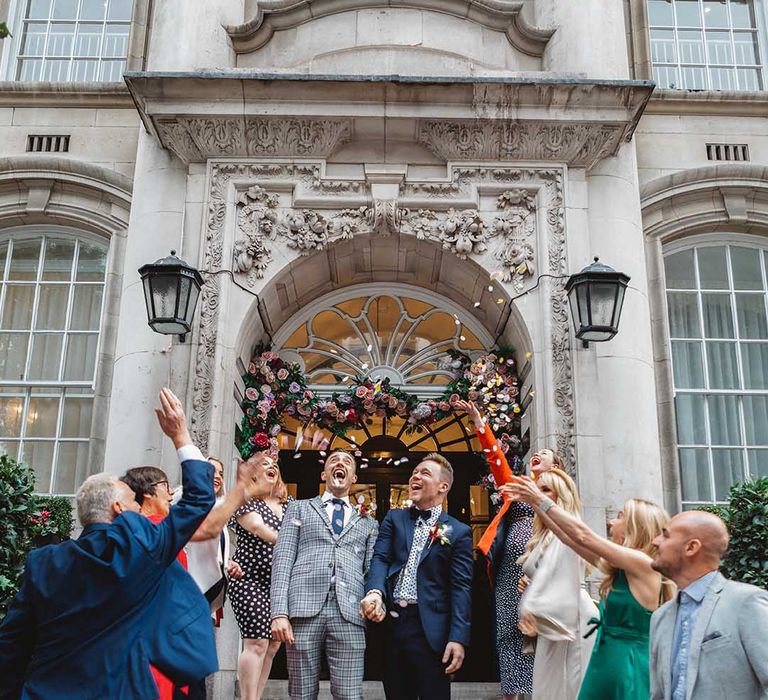 Grooms stand on Chelsea Old Town Hall steps outdoors as confetti is thrown around them