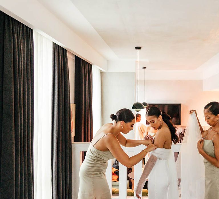 Bridesmaids in sage green satin dresses with bridesmaids helping the bride with finishing touches