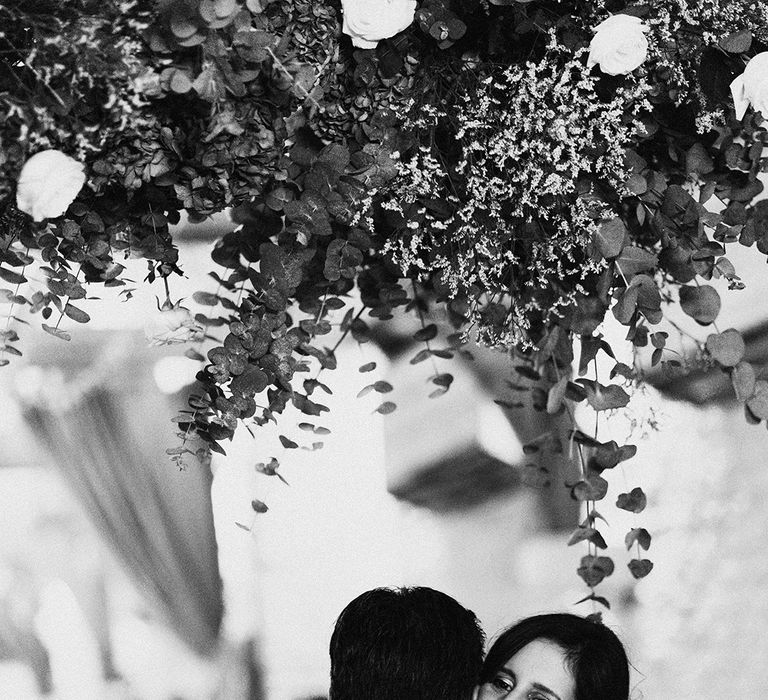 Bride smiles under flower cloud as she hugs the groom 