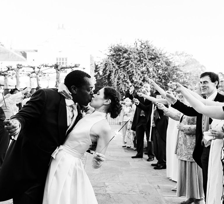 Bride and groom share a kiss as they and the wedding guests wave sparklers