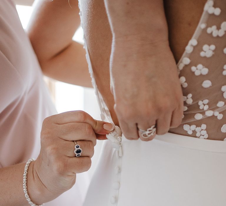 Mother of the bride helps the bride into her wedding dress with mesh back and dot design