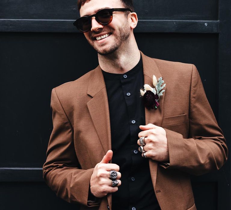 Groom in sunglasses, black shirt and brown jacket at retro wedding 