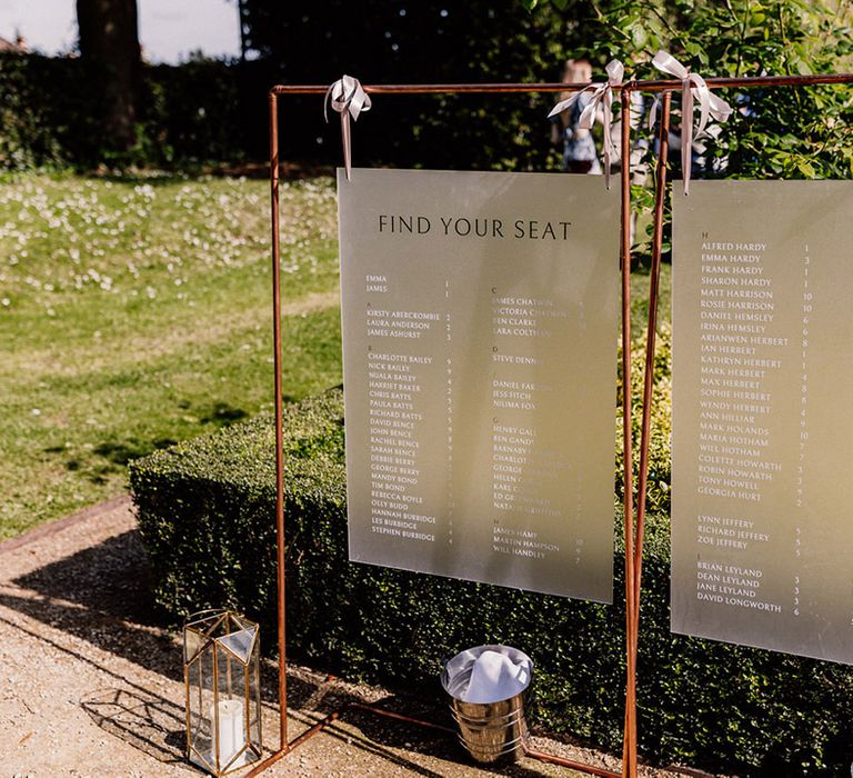 Frosted seating chart and table plan on copper frame decorated with white ribbons and candles in geometric lanterns 