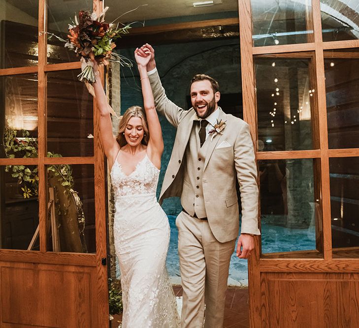 Bride & groom walk into wedding reception in the Villa Catignano in Tuscany as they lift their arms in the air 