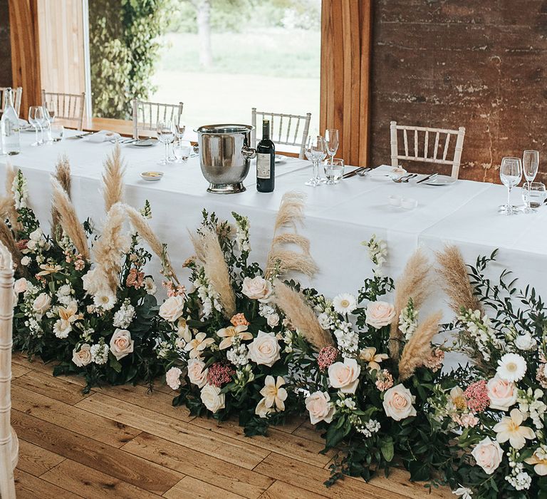 Blush pink flowers and pampas grass floral arrangements line the top table 