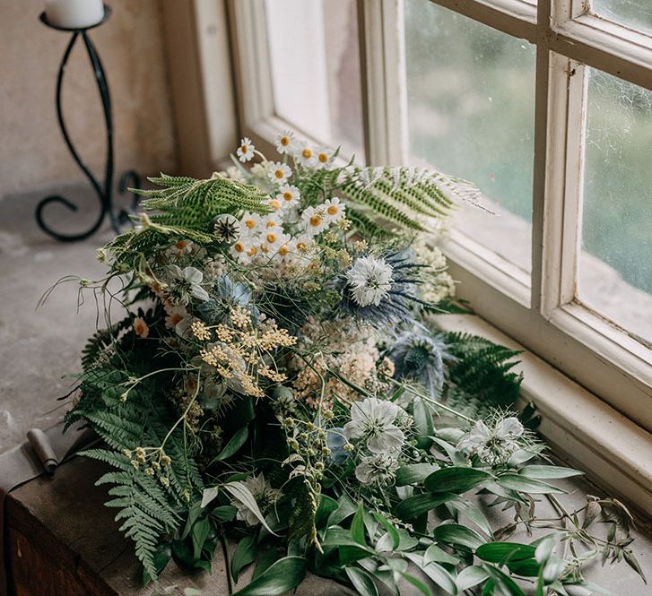 Brides oversized floral bouquet filled with daisies and greenery lays on windowsill 