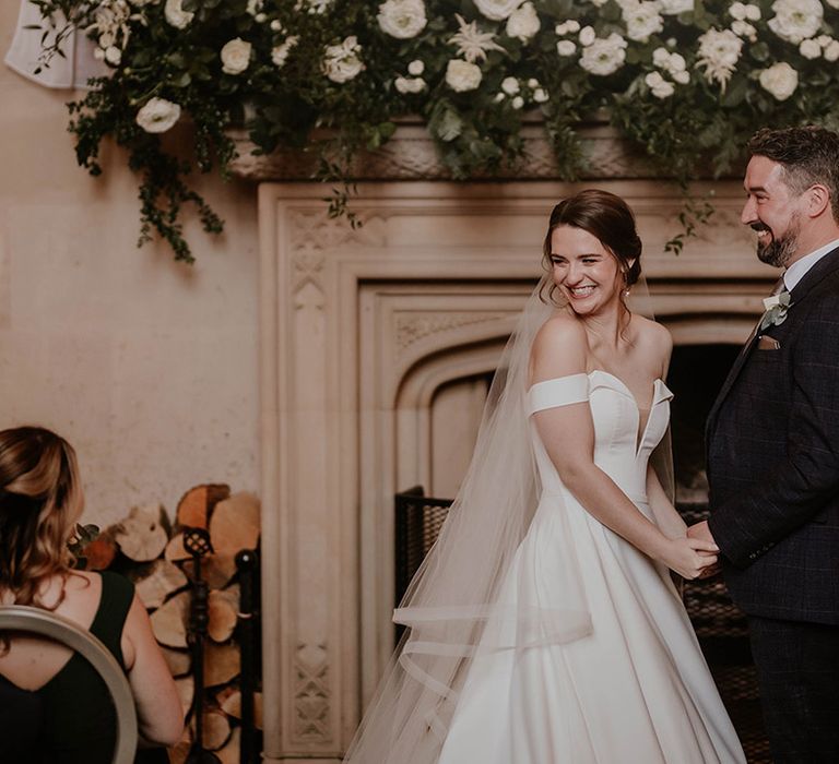 Bride and groom holding hands smile and turn to look at their guests during the ceremony 