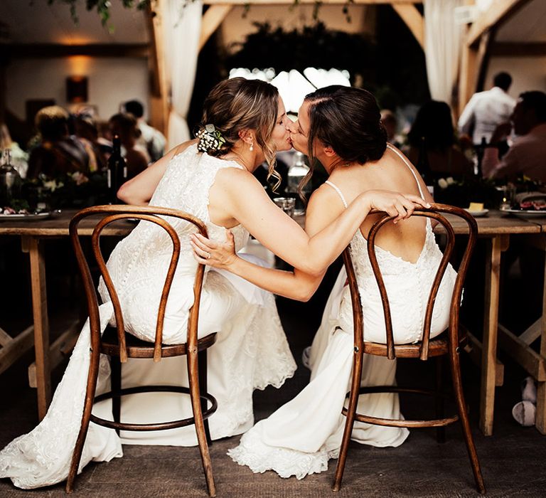 Brides seated for their wedding reception share a kiss 