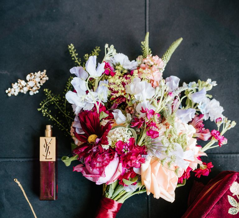 Bright floral bridal bouquet tied with bright pink ribbon beside YSL bridal perfume 