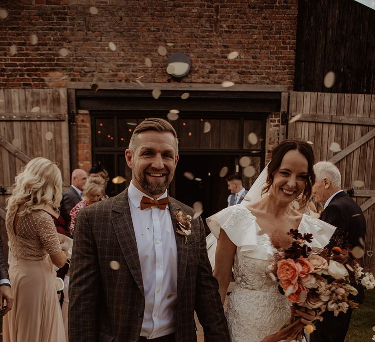 Groom in a grey checkered suit with a bow tie and bunny grass buttonhole with the bride in a custom Emma Beaumont Atelier embroidered dress