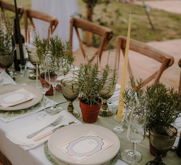 Tall yellow taper candles on a white and green tablescape with green coloured glassware and cream plates 