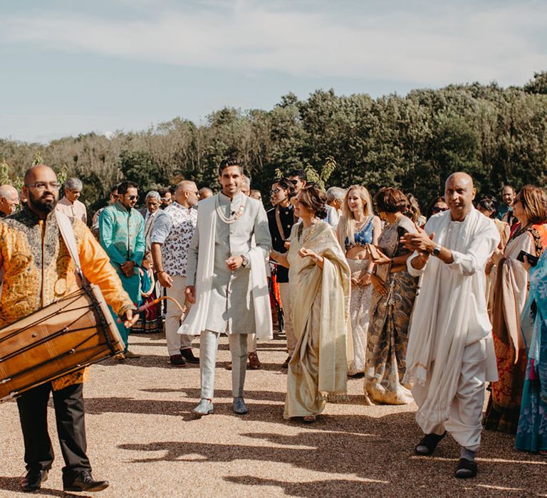 Groom walks with wedding party in colourful outfits for traditional Indian wedding ceremony 