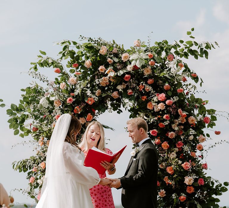 Bride & groom marry at Botley Hill Barn in front of floral archway 