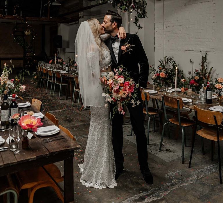 Bride and groom standing in Hackney Studios wedding reception with large hanging foliage decoration, fairy lights and neutral wedding tablescapes 