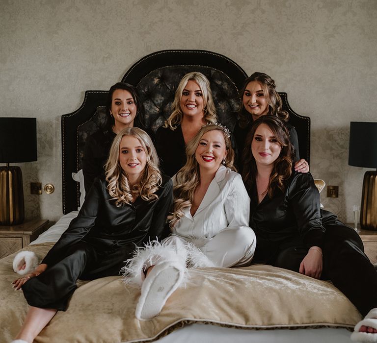 Bride in white silk two piece pyjamas with feather trimmed hem and white fluffy slippers and bridesmaids in matching black silk two piece pyjamas