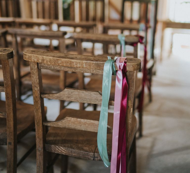 Wooden chairs in wedding reception room with baby blue, baby pink and deep pink ribbons tied on