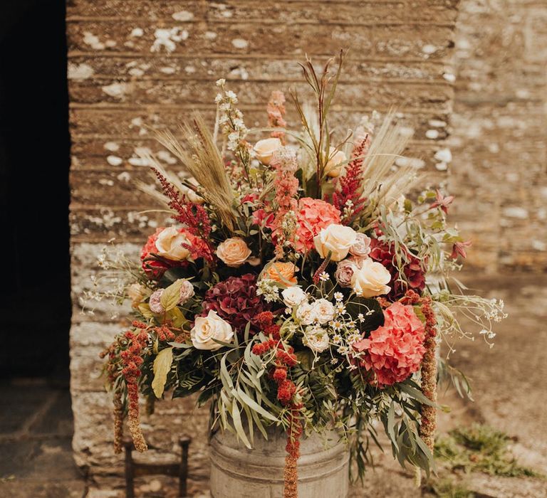 Light red and dark red hydrangeas with white and orange roses in a milk churn 