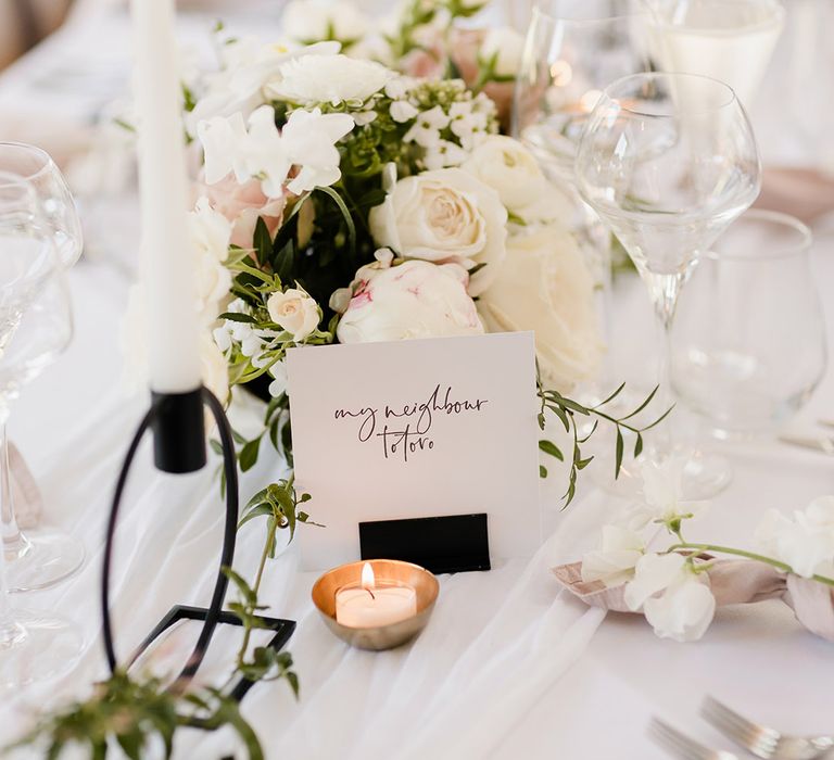 White fabric table runner and white floral bouquet complete with tea lights in brass holder