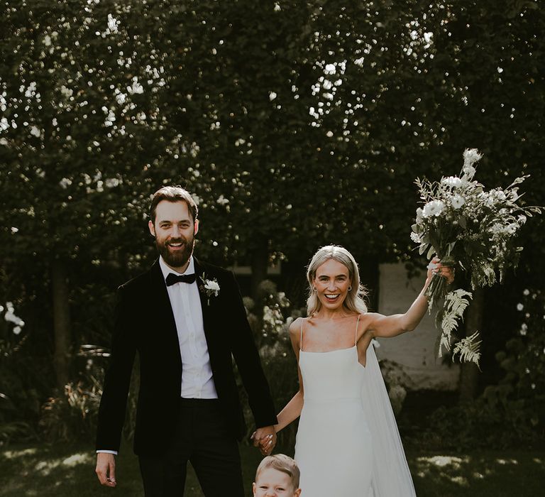 Cute page boys in bow ties and braces posing with the bride in a fitted wedding dress and from in black tuxedo for classic style wedding 