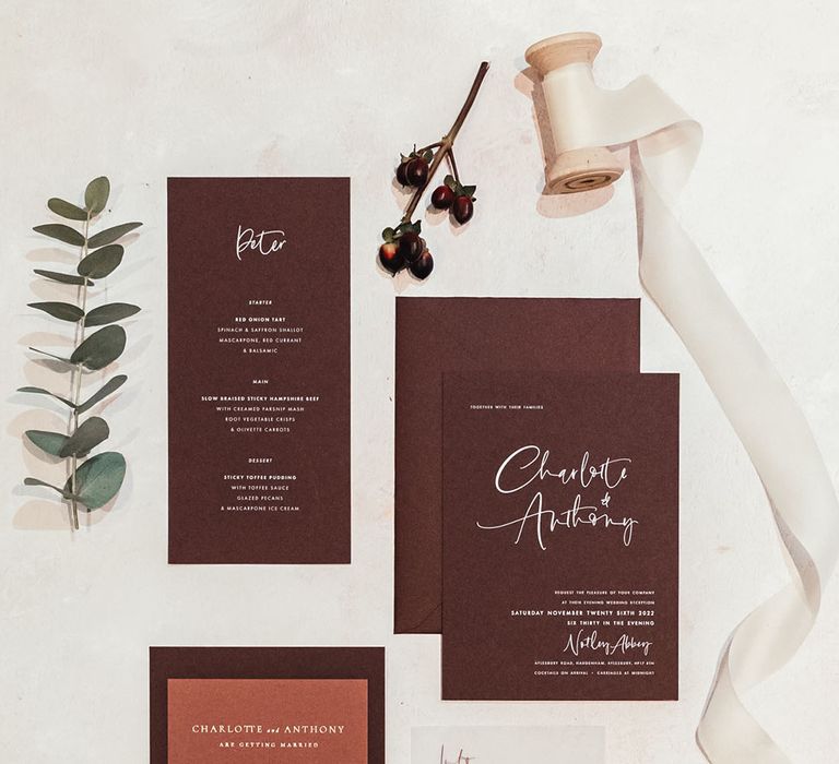 Deep burgundy wedding stationery flatlay with white accents and frosted paper with ribbon 