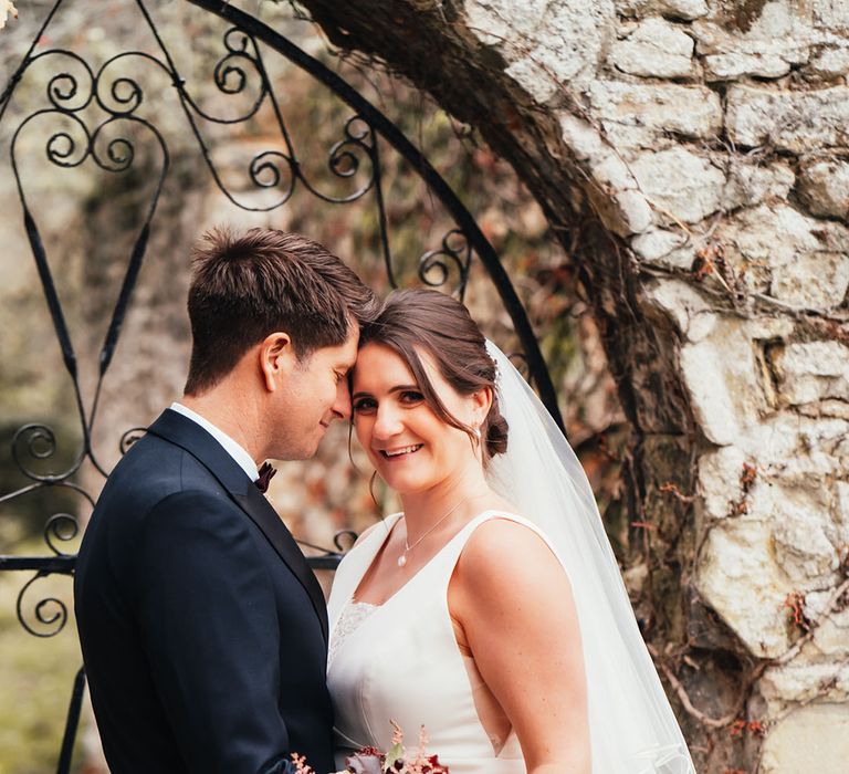 Bride in a traditional white wedding dress holding a dark red and white bouquet posing with the groom for their couple portraits at Notley Abbey