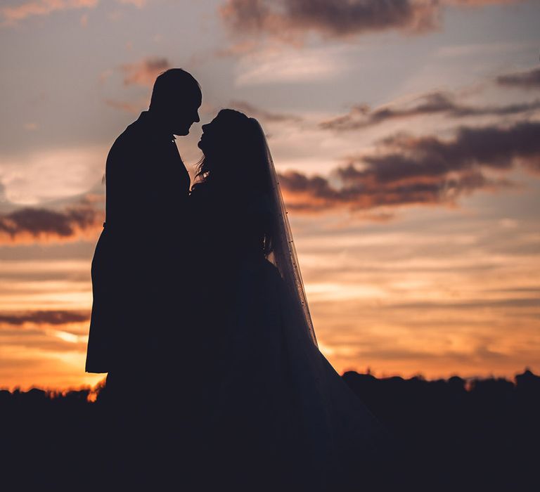 The sun is almost set with the bride and groom sharing an intimate moment and looking into each other's eyes with the bride wearing a pearl veil 