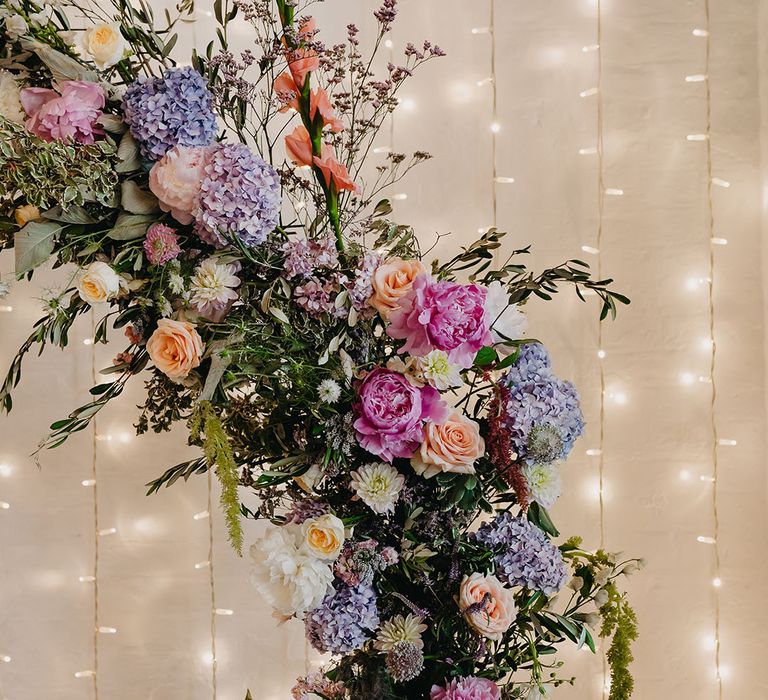 Pastel seasonal floral arch beside fairy light curtain