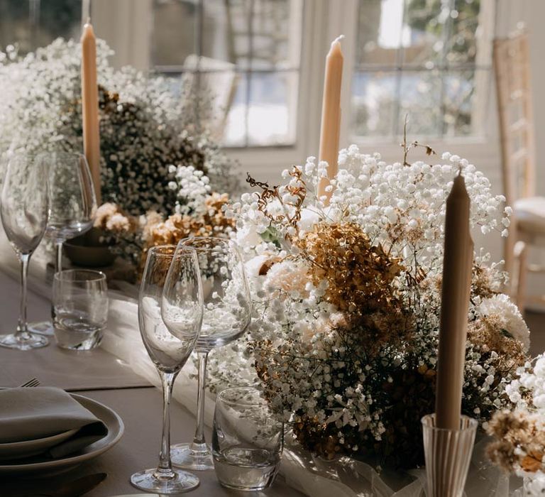 Minimalistic luxe wedding tablescape with clean, soft neutrals, a tulle tablerunner, neutral tapered candles and large neutral coloured baby's-breath table arrangements 