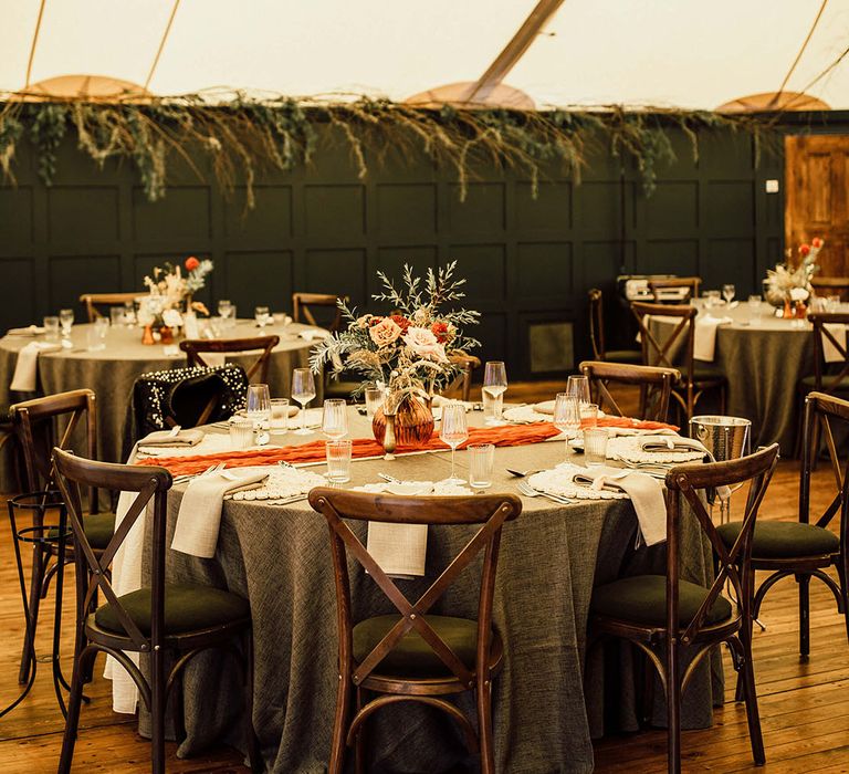 Hanging green foliage installation above round tables with green tablecloths and orange table runners 